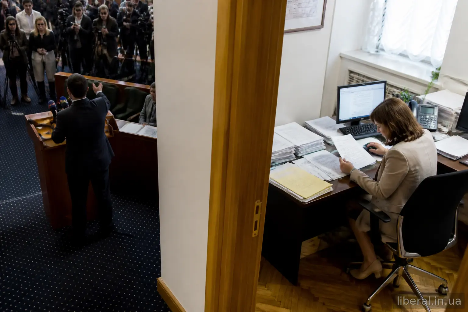 Політик виступає перед мікрофонами, а державний службовець працює з документами в кабінеті